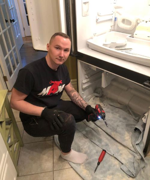 Max Appliance Repair technician repairing fridge with tools in hand