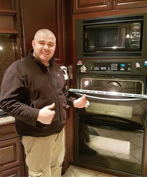 technician standing next to newly repaired oven with thumbs up